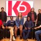 Spring 2026 acting graduates, some sitting in chairs some standing behind them, with the KD Studio logo on a large TV screen behind them.